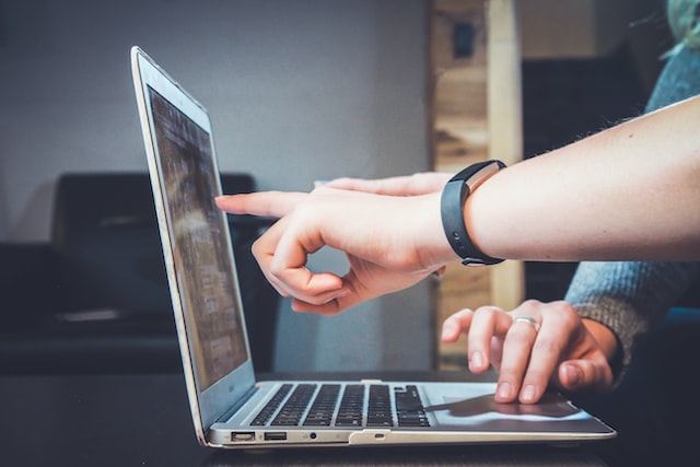 Person pointing at laptop screen while another person scrolls