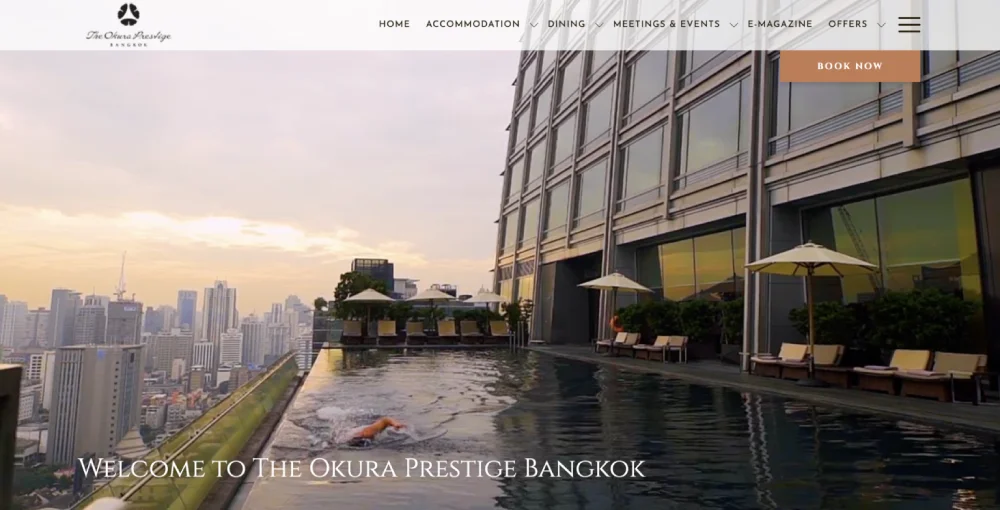 A person swims in a rooftop pool at The Okura Prestige Bangkok, overlooking the city skyline, a view as captivating as the hotel's renowned best website design.