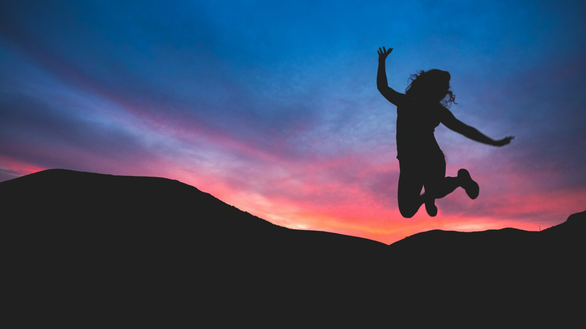 woman jumping in front of a mountain at dusk